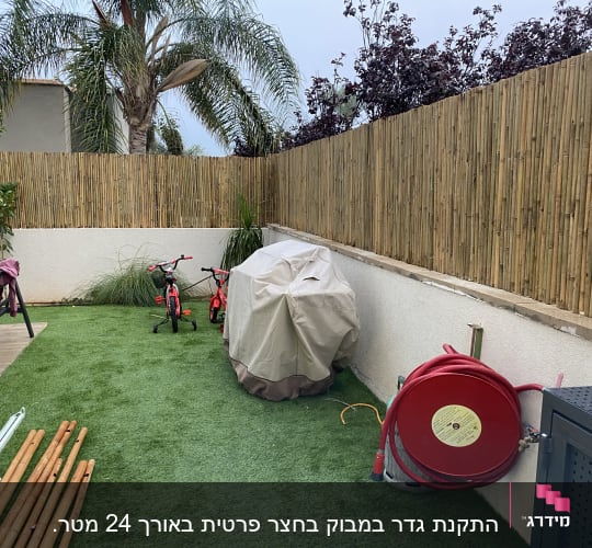 גדר במבוק בגינה עם צינור מים אדום